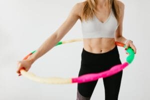 crop sportswoman exercising with gymnastic hula hoop