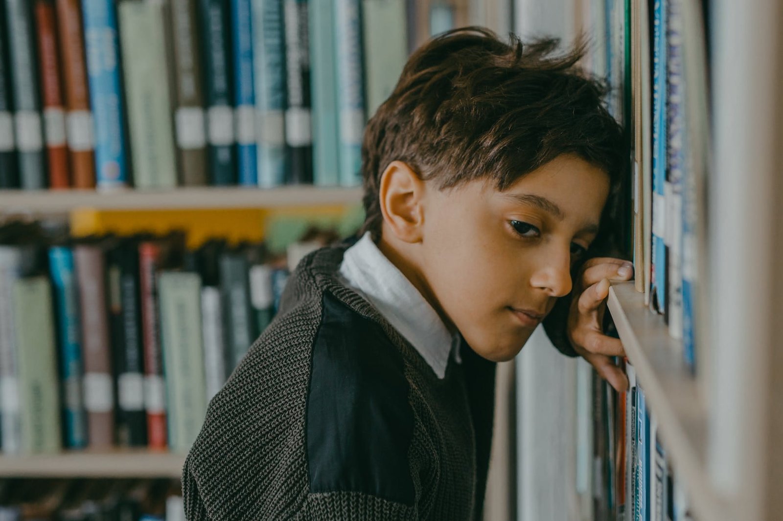 photo of a boy leaning against bookshelves
